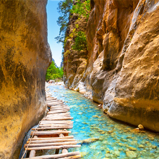 Smal wandelpad door de Samariakloof, met houten loopplanken langs een heldere rivier tussen hoge, rotsachtige kloofwanden.